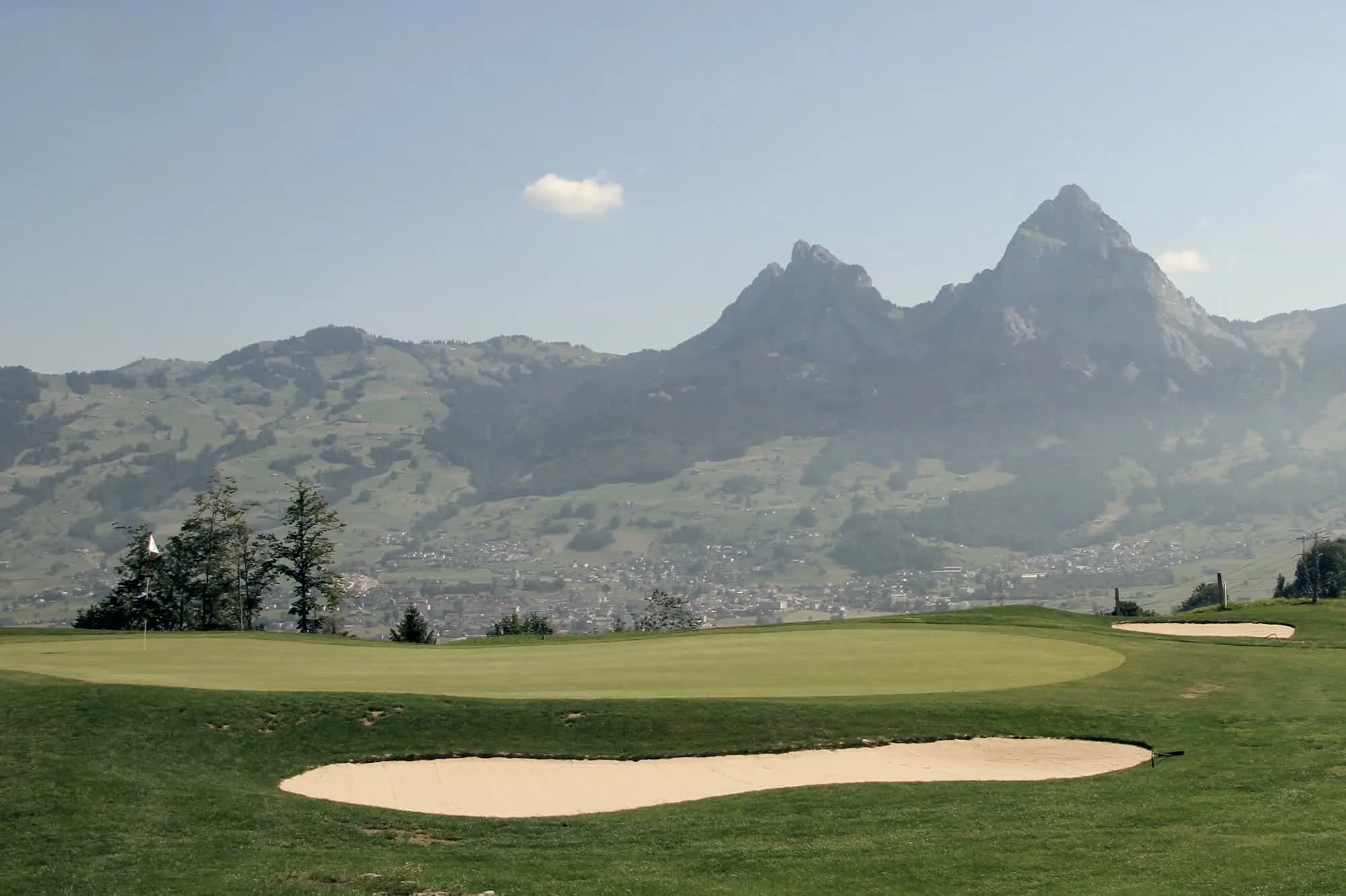 A putting green and bunker, the Mythen peaks hazy behind it.