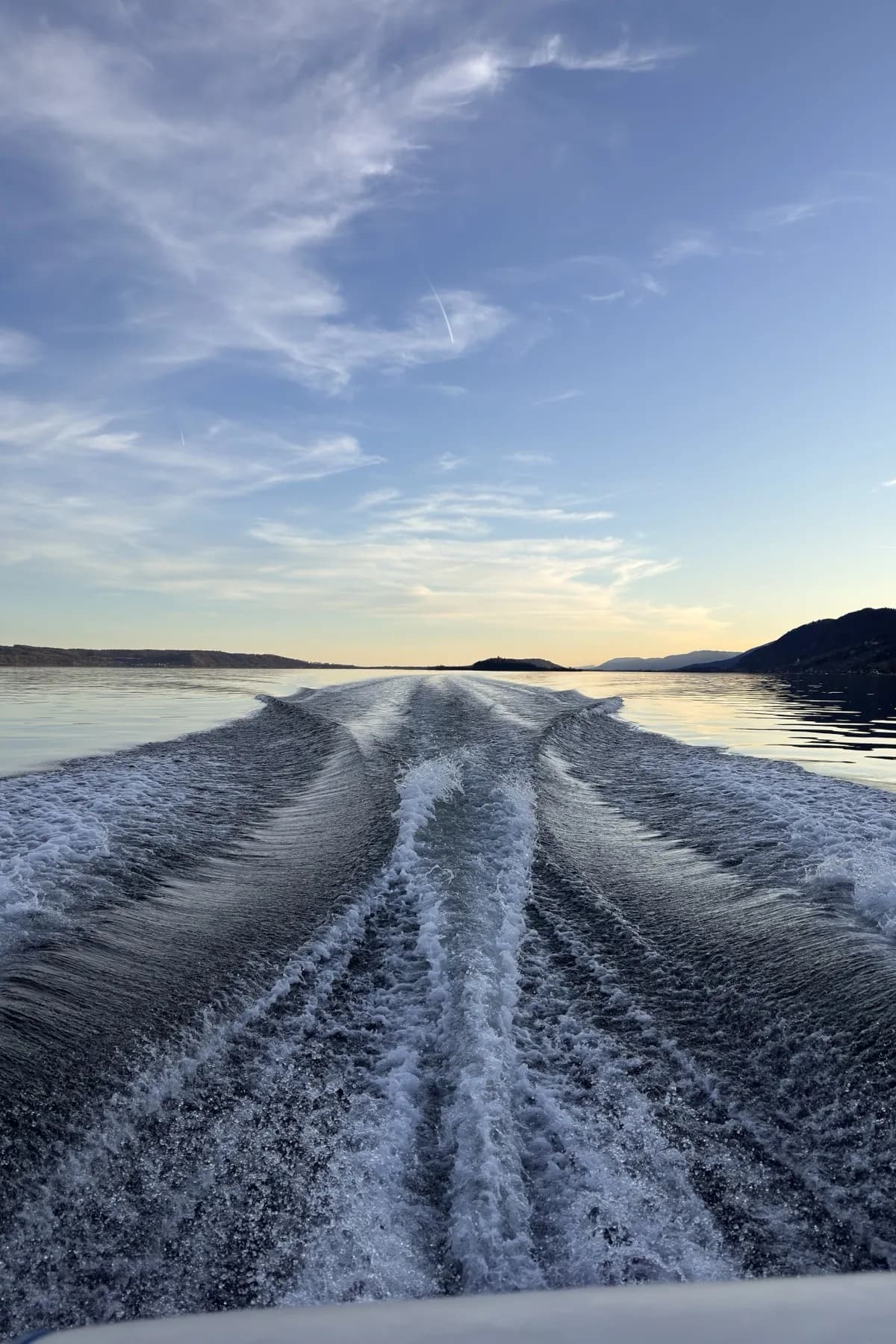 A boat's wake on open water, an island on the horizon behind it.
